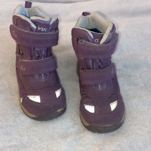 Lila vinterkängor från Viking strl 27 - Säljer ett par lila vinterkängor från Viking i storlek 27. Skorna har två kardborreband, reflexdetaljer och är fodrade för extra värme. Yttermaterialet är slitstarkt och vattentätt Gore-Tex, perfekt för kalla dagar. Sulan är rejäl och greppvänlig.