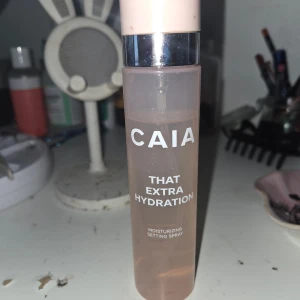 CAIA That Extra Hydration Setting Spray - Återfuktande setting spray från CAIA i en snygg rosa plastflaska med silvrig detalj och ljusrosa lock. Perfekt för att ge huden extra fukt och fixera sminket hela dagen. Enkel att spraya över ansiktet för en fräsch finish.