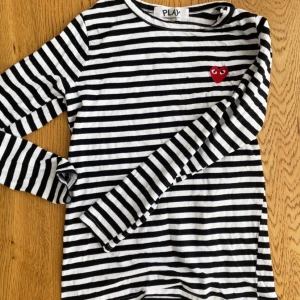 Randig långärmad tröja Comme des Garçons - Säljer str L Kids så mer som en XS svartvit randig långärmad tröja från Comme des Garçons Play. Tröjan har det ikoniska röda hjärtat broderat på bröstet och är gjord i mjuk bomull. Perfekt för dig som gillar stilrena och trendiga plagg med en twist.