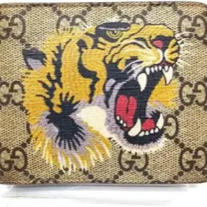Gucci plånbok med tiger och GG-mönster (Äkta) - Snygg plånbok från Gucci med klassiskt GG-mönster i beige och brunt. Framsidan har en fet broderad tiger i gult, svart och vitt som verkligen sticker ut. Insidan är svart skinn med flera kortfack. Perfekt för dig som vill ha något unikt och lyxigt i fickan.