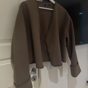 Brun kofta från Gina Tricot - Säljer en brun kofta från Gina Tricot med snygga synliga sömmar längs kanterna och breda, långa ärmar. Storlek XS. 