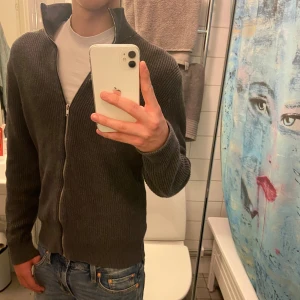 Mörkgrå full zip - Säljer en mörkgrå full zip från East West i storlek M. Tröjan är i väldigt bra skick och har en stilren passform, tveka inte på att höra av dig om du har några frågor.