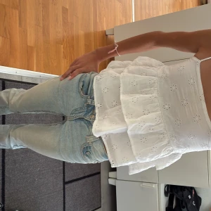 Vit volangtop från Gina Tricot - Supersöt vit topp från Gina Tricot med tunna axelband och broderade blommor. Toppen har två lager volanger och är gjord i bomull, perfekt för varma dagar. Sitter löst och luftigt med en sommar vibe💗💗