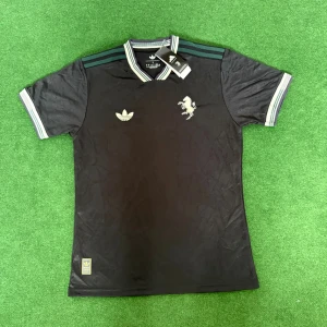 Juventus 25/26 Adidas svart fotbollströja - Juventus x Adidas svart fotbollströja med diskret bladmönster i tyget, broderad vit Juventus-logga och Adidas Trefoil på bröstet. Gröna ränder på axlarna och ribbade muddar i vitt och grönt. Tillverkad i glansigt, lätt polyestermaterial.