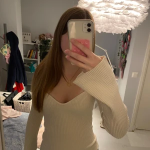 Ribbad v-ringad beige tröja - Säljer en ribbad beige tröja med v-ringad hals och långa ärmar. Tröjan har en figurnära passform och vida ärmslut som ger en snygg och trendig look. Perfekt att styla med jeans eller kjol för en stilren outfit.