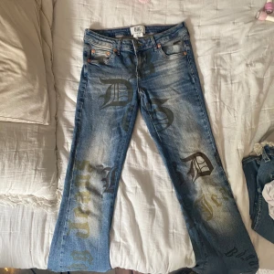 BDG blå jeans med tryck, 27W 32L - Säljer ett par blå jeans från BDG Urban Outfitters med coolt tryck i svart och gult över hela byxorna. Jeansen har klassisk femficksdesign, raka ben och låg midja. Materialet är jeans i bomull och passformen är normal. Perfekta för dig som vill sticka ut.