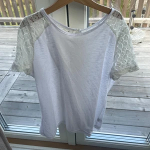 Vit blus med spetsärmar och knappar - Säljer en söt vit blus med korta ärmar i spets och fina knappar i ryggen. Blusen har rund halsringning och spetsdetaljer över axlar och övre rygg. Perfekt för dig som gillar romantiska och feminina detaljer.