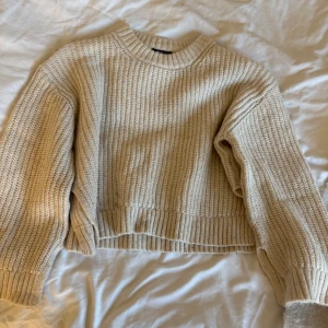 Beige stickad tröja från Gina Tricot - Supermysig beige stickad tröja från Gina Tricot med grov ribbad struktur och rund hals. Tröjan har långa ärmar och breda muddar vid ärmslut och nederkant. Perfekt för lager-på-lager och chill dagar. Passar dig som gillar enkel och clean stil.