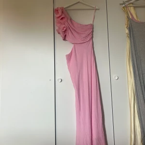 Ljusrosa långklänning oneshoulder - Säljer en ljusrosa långklänning med oneshoulder och volangdetaljer vid axeln. Klänningen har smal axelrem och en elegant, draperad överdel. Passar perfekt till balen eller till andra fina tillfällen. Ber om ursäkt för den dåliga bilden men det är bara att skicka om ni vill ha ny bild!! Den är aldrig använd men prislappen är fortfarande kvar!🩷🩷