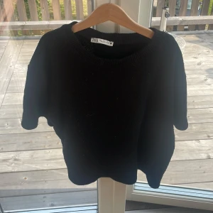 Svart stickad tröja från Zara - Svart stickad tröja från Zara med korta ärmar och rund halsringning. storlek L men sitter som xs/s. Tröjan har en enkel och clean design, perfekt att styla med jeans eller kjol. Mjuk och skön känsla tack vare det stickade materialet.