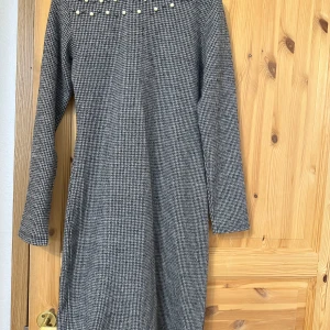 Grå rutig klänning med pärlor - Snygg klänning i grått och vitt rutigt mönster med lång ärm. Upptill finns dekorativa pärlor som ger en cool touch. Klänningen har rak passform, storleken är large men passar mest medium.