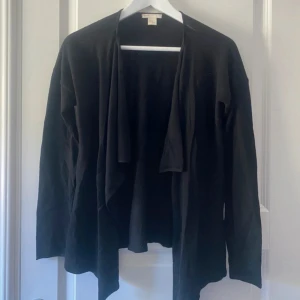 Svart kofta med öppen front - En svart, långärmad kofta från Boob med öppen front och avslappnad passform. Tunn och mjuk, perfekt att slänga över en t-shirt eller topp. Enkel och stilren design som funkar till många outfits.