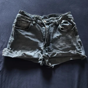 Grå jeansshorts med broderade fickor - Säljer ett par grå jeansshorts med råa kanter och slitna detaljer. Shortsen har klassisk femficksdesign och bakfickorna är dekorerade med broderade vingar. Dom är storlek Medium men dom passar som Small. 