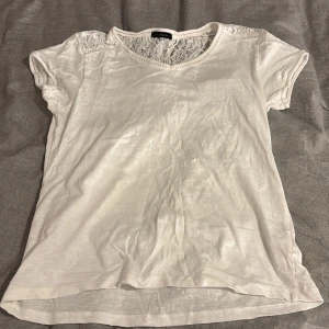 Vit blus med spets från Mana - Supersöt vit blus från Mana i storlek S. Toppen har korta ärmar och v-ringning, med fina spetsdetaljer över axlar och rygg. Tillverkad i mjukt material som känns skönt mot huden. Perfekt för dig som gillar romantiska och feminina detaljer.