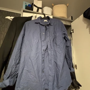 Blå skjorta från Filippa K - Snygg blå skjorta från Filippa K i klassisk modell med knappar hela vägen och bröstficka. Skjortan är långärmad och tillverkad i mjuk bomull, perfekt för en clean och stilren look.