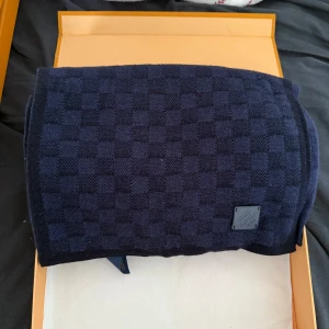 Mörkblå rutig halsduk Louis Vuitton - Snygg mörkblå halsduk från Louis Vuitton med klassiskt rutigt mönster och diskret logotyp i hörnet. Halsduken är stickad och har en lyxig känsla, perfekt för att lyfta din outfit under kyliga dagar. Använd typ 1 gång. Vid frågor kontakta mig. 