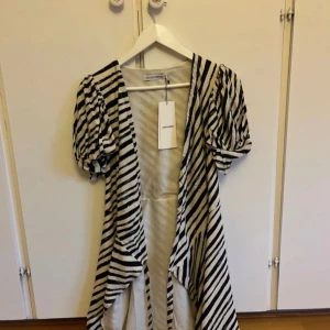 Zebramönstrad klänning från Adoore - Supersnygg kort zebramönstrad klänning från Adoore med puffiga korta ärmar och v-ringning. Klänningen är svart och vit med diagonala ränder och har en flowy passform som ger en cool och trendig look. Perfekt för dig som vill sticka ut med stil. Aldrig använd och prislapp kvar. 