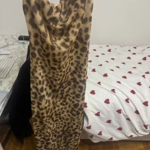 Leopardmönstrad långklänning från Zara - Säljer en snygg långklänning från Zara med leopardmönster. Klänningen har en lös passform och är ärmlös med snygg draperad urringning. Perfekt för dig som vill sticka ut med ett djurmönster och gillar trendiga vibes.