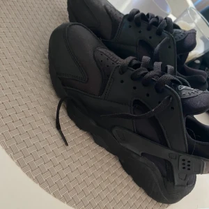 Svarta Nike Air Huarache sneakers - Säljer ett par helsvarta Nike Air Huarache sneakers. Skorna har en mix av textil och syntetmaterial, snörning och en stabil hälkappa i gummi. Perfekta för dig som gillar en sportig och clean look. Använda 2 gånger:) 