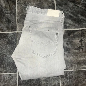 Replay jeans  - Snygga ljusgrå jeans från Replay med klassisk femficksdesign och diskret Replay-logga på bakfickan. Jeansen har slim fit-passning och raka ben. JAG SKICKAR EJ FLER BILDER NÄR JAG BÄR JEANSEN! för storleksguide hänvisar jag till måtten och för bättre inblick i passformen rekommenderar jag att googla på modellnamnet. Jeansen kan vara uppsydda utan att jag noterat det så kolla måtten noggrant :) Midja 46cm, längd 100cm. OBS se defekt på sista bilden. 39