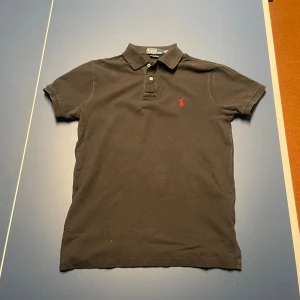 Svart pikétröja från Ralph Lauren - Klassisk svart pikétröja från Ralph Lauren med röd broderad logga på bröstet..