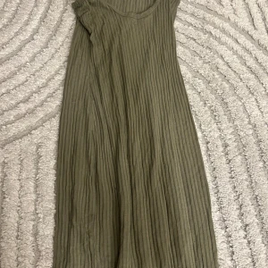 Olivgrön ribbad klänning Gina Tricot - Säljer en olivgrön ribbad långklänning från Gina Tricot. Klänningen har smala axelband och ärmlös design, med en mjuk och stretchig känsla. Perfekt för dig som gillar enkel och stilren look med en twist av struktur.