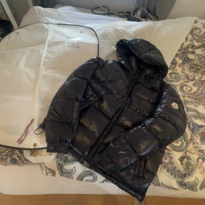  Moncler maya (navy) - Säljer en navy pufferjacka från Moncler med glansig finish och huva. Jackan har dragkedja framtill, två sidofickor och klassisk Moncler-logga på ärmen. Perfekt för kalla dagar och riktigt snygg streetstil. Passar tyvärr inte mig