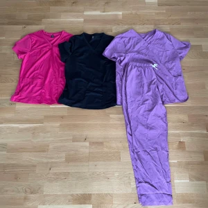 Tre färgglada kortärmade tröjor + ett par byxor  - Säljer tre kortärmade tröjor med v-ringning och stora fickor framtill. En är knallrosa, en svart och en lila. Perfekta för dig som gillar bekväma och stilrena basplagg. Den lila tröjan kommer med matchande byxor med dragsko i midjan.