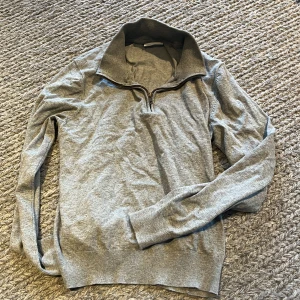 Grå half zip tröja från Grunt ungdom - Snygg grå långärmad tröja från Grunt i storlek L. Tröjan har en hög krage med half zip-dragkedja och är tillverkad i mjukt bomullsmaterial. Perfekt för chill dagar och enkel att matcha med jeans eller joggers.