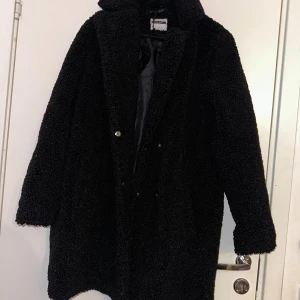 Svart teddyjacka från Noisy May - Mysig svart teddyjacka från Noisy May med fluffig yta och klassisk krage. Jackan har långa ärmar och knäppning framtill. Perfekt för dig som gillar oversized och chill stil under höst och vinter.