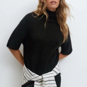 Svart polotröja från Gina - Svart polotröja med korta ärmar och hög krage. Tröjan är stickad och har en mjuk, lite luddig yta som ger en mysig känsla. Perfekt för lager-på-lager och funkar till både jeans och kjol aldrig använt❤️