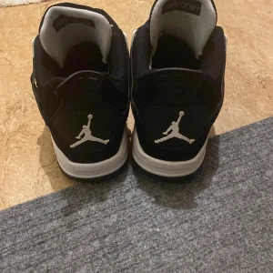 Svarta Nike Air Jordan 4 sneakers - Säljer ett par svarta Nike Air Jordan 4 sneakers med vita detaljer och Jumpman-logga på hälen och plösen. Skorna har snörning, meshpaneler och en platt sula. Stilren design med kontrasterande vita inslag och klassisk siluett som sticker ut. Kom privat finns erbjudanden på skorna det ingår även en till vara me kom privat för mer information 