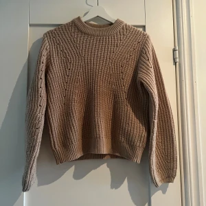 Beige stickad tröja från Gina Tricot XS - Supermysig beige stickad tröja från Gina Tricot med snyggt strukturmönster och rund hals. Tröjan har långa ärmar och breda muddar vid ärmslut och nederkant. 