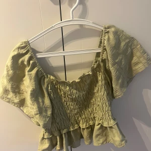 Ljusgrön croppad blus med volang - Säljer en ljusgrön blus med croppad passform och volangkant nedtill. Toppen har korta, puffiga ärmar och är smockad över bröstet för en snygg och bekväm look. Perfekt för dig som gillar romantiska detaljer och en chill vibe. M men sitter mer som S ❤️