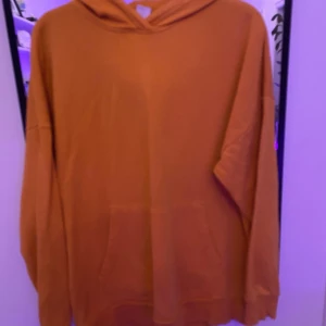 Orange hoodie från Lindex med tryck - Cool orange hoodie från Lindex med stor FUTURE-tryck i vitt och svart på ryggen. Tröjan har huva, känguruficka och lång ärm. Oversized passform som ger en chill vibe. Tillverkad i mjuk bomull, perfekt för att hänga med kompisar.