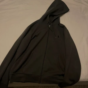 Grå hoodie från Polo Ralph Lauren - Grå hoodie från Polo Ralph Lauren med dragkedja framtill och klassisk huva. Tröjan har två fickor på magen. Perfekt för vardagardagar och enkel att matcha med allt. Mjuk och skön bomullskänsla. Pris kan diskuteras vid snabb affär. Köpt för 1800