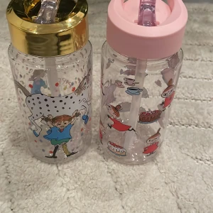 Mumin och Pippi Långstrump vattenflaskor med sugrör - Två fina vattenflaskor med sugrör, en med Pippi Långstrump-motiv och guldfärgat lock, en med Mumin-karaktären Lilla My och rosa lock. Båda är i mycket gott skick, inga synliga repor eller skador. Perfekt för barn eller samlare av nordiska klassiker. OBS dem är ej andvända! 