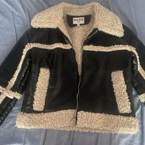Svart teddyjacka från NA-KD - Säljer en svart teddyjacka från NA-KD med krage och detaljer i beige teddyfleece. Jackan har dragkedja framtill, två fickor och coola kontrasterande paneler. Perfekt för dig som vill ha en trendig och mysig look i höst och vinter. Väldigt varm, har två st.