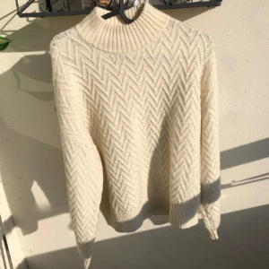 Vit stickad polotröja med mönster - Supermysig vit stickad polotröja med snyggt mönster. Tröjan har hög krage och långa ärmar med ribbade muddar. Den är S men passar M oxå