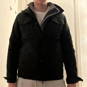 Mörkgrön jacka från John Henric - Säljer en mörkgrön jacka från John Henric med quiltat foder och flera fickor framtill. Jackan har både dragkedja och knappar, samt en hög krage som ger extra stilpoäng. Perfekt för dig som gillar en clean och klassisk look.