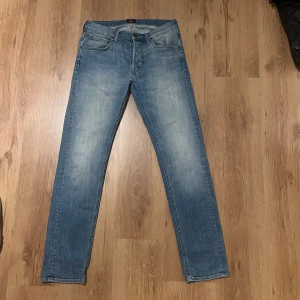 Blå Lee jeans 30/32 - Snygga ljusblå jeans från Lee med klassisk femficksdesign och raka ben. Jeansen har normal passform och är tillverkade i mjukt bomullsmaterial. Faded tvätt ger en cool och avslappnad vibe. Perfekt för dig som gillar stilrena och tidlösa jeans. Midja 40cm längd 106cm (76)