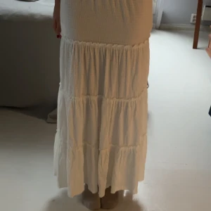 Vit långkjol med volanger från Reserved - Luftig och snygg vit långkjol från Reserved i storlek S. Kjolen har flera volanglager och resår i midjan för en bekväm passform. Perfekt för varma dagar och ger en bohemisk vibe. Materialet känns mjukt och lätt.