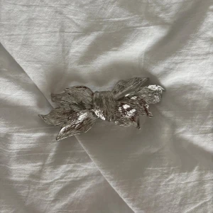 Silvrig hårklämma i form av rosett - Snygg hårklämma i silverfärgad metall med en cool rosettform och texturerad yta som ger extra glans. Perfekt för att ge din frisyr en unik touch och passar till alla hårtyper. Klämman är rejäl och håller håret på plats hela dagen.