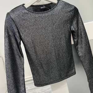 Glittrig silver långärmad topp Gina Tricot - Säljer en snygg långärmad topp från Gina Tricot i glittrigt silver. Toppen har rund halsringning och är figurnära i modellen. Perfekt för dig som vill sticka ut med lite extra shimmer. Materialet är mjukt och stretchigt syntet som sitter skönt mot kroppen. Strl XXS/XS