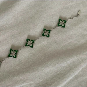 Grönt och silver armband med blommor - Snyggt armband med fem blommiga länkar i grönt och silver. Blommorna har en fyrklöverform och sitter på en tunn silverkedja. Perfekt för dig som gillar färg och unika detaljer. Armbandet oanvänd, jag tror att det är storlek xs/s