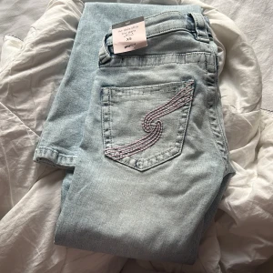 Ljusblå ultra low jeans Gina Tricot - Säljer ett par ljusblå ultra low jeans från Gina Tricot i storlek XS tall. Modellen har klassisk femficksdesign, broderad bakficka med rosa detaljer och raka ben. Jeansen är tillverkade i mjukt bomullsmaterial och har låg midja för en trendig look.