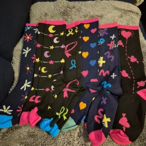 Färgglada mönstrade stöd strumpor, 6-pack - Säljer ett 6-pack strumpor med olika mönster som hjärtan, blommor, stjärnor, månar och symboler. Färgerna är blandade med svart, blå, rosa, gul, grön och orange. Strumporna har kontrastfärgade tår och muddar i rosa, blå och grönt. Perfekt för dig som gillar färg och roliga detaljer.