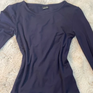 Mörkblå långärmad topp Gina Tricot - Säljer en stilren mörkblå långärmad topp från Gina Tricot i storlek XXS. Toppen har en rund halsringning och är figurnära i passformen. Perfekt att matcha med jeans eller kjol för en clean look. Materialet är mjukt och stretchigt, troligtvis bomull eller polyester.