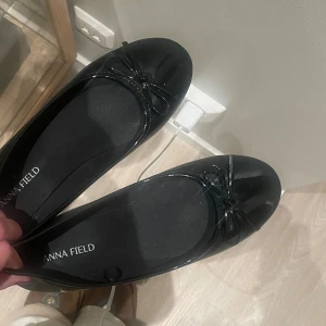 Svarta ballerinaskor från Anna Field - Snygga svarta ballerinaskor från Anna Field med glansig finish och en söt rosettdetalj framtill. Skorna har rund tå och platt sula, vilket gör dem bekväma att bära hela dagen. Perfekt för dig som gillar stilrena och klassiska skor med en feminin touch. Använda en gång