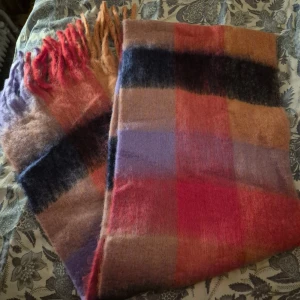 Rutig fluffig halsduk i varma färger - Stor och supermjuk halsduk med rutigt mönster i lila, rosa, röd, beige och mörkblå toner. Halsduken har långa fransar i ändarna och en fluffig, cozy känsla som gör den perfekt att svepa in sig i under kyliga dagar.